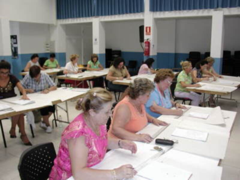 Estudiantes en una aula de clase, sentados en mesas y trabajando con libros y cuadernos.