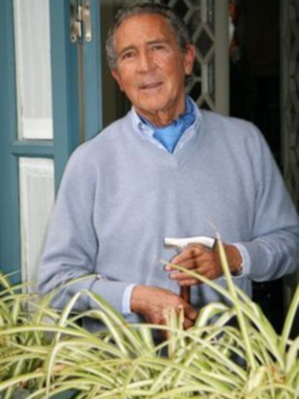 Un hombre en una puerta de casa, sosteniendo un control remoto. La imagen muestra una escena casual y relajada. El hombre parece estar en un momento de descanso o de estar en casa. La puerta de fondo sugiere que se encuentra en un entorno residencial.