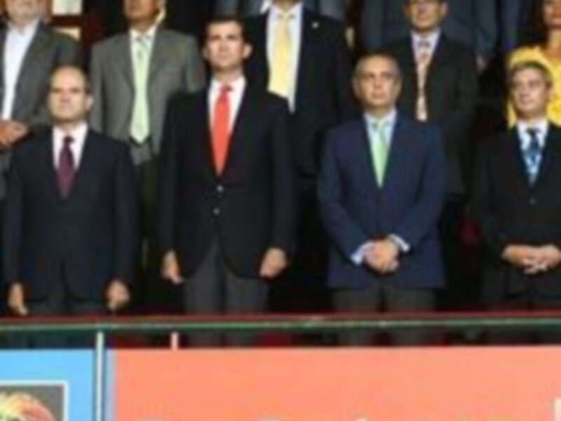 Una imagen de una conferencia de prensa con varios hombres en trajes, algunos sonríen y otros miran hacia adelante. En el fondo hay un escudo de la EuroBasket 2007, lo que sugiere que se trata de una reunión relacionada con el baloncesto europeo.