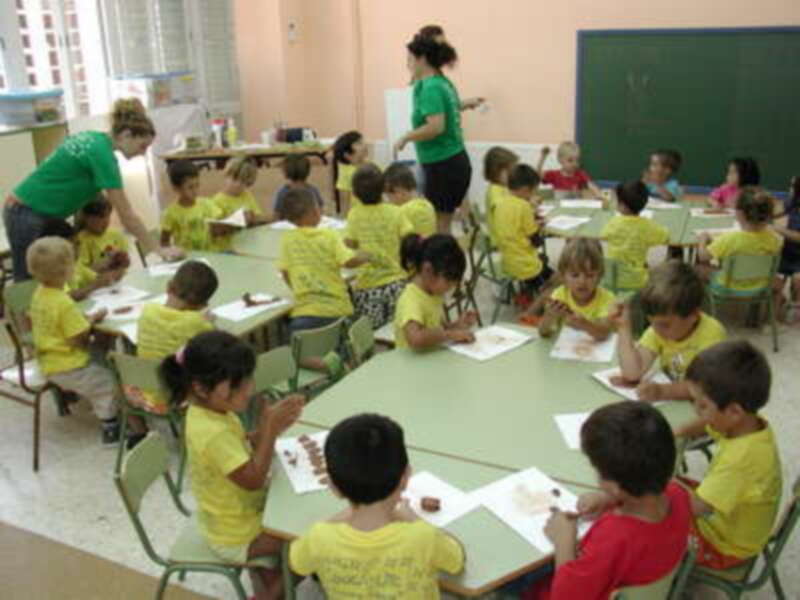 Niños en una clase de primaria, con maestras enseñando y niños escribiendo en sus cuadernos.
