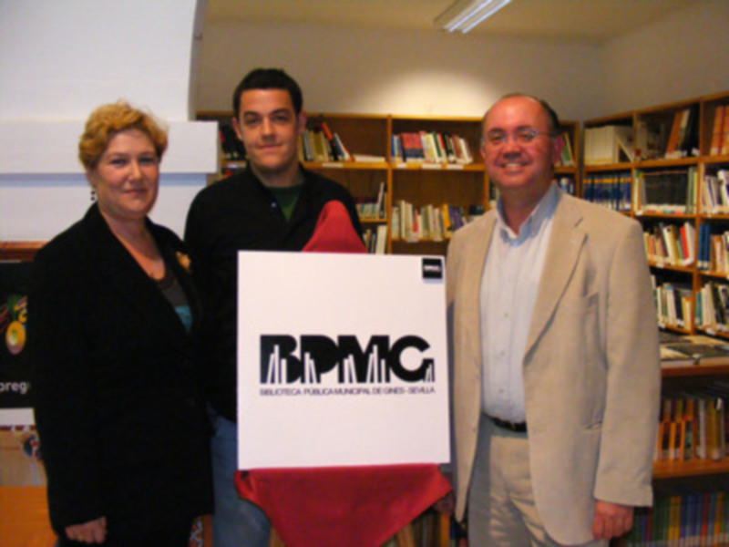 Tres personas posan frente a un cartel con el logo de 'BPMG' en una biblioteca.