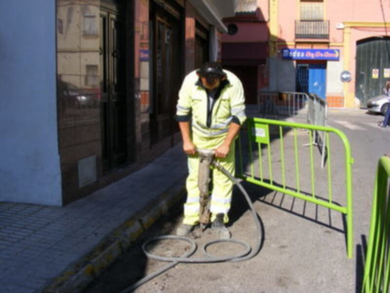 Trabajador en uniforme de seguridad perforando con una herramienta hidráulica en una calle urbana.