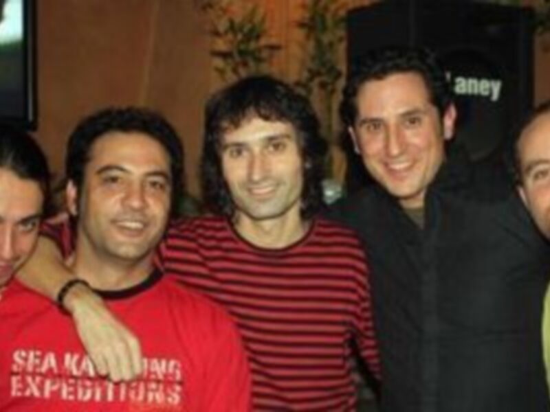 Un grupo de amigos posando juntos en una sala, con uno de ellos usando un jersey rojo y otro con una camiseta amarilla.