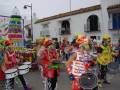 Desfile de carnaval con músicos en trajes coloridos tocando tambores y instrumentos de percusión en una calle decorada.
