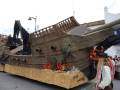 Barco de madera decorativo en un desfile, con detalles náuticos y figuras de marinero.