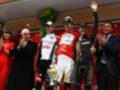 Triunfo en el Giro de Italia 2011: El ciclista HTC-Fastweb celebra su victoria en el podio, rodeado de sus compañeros de equipo y la organización del evento.
