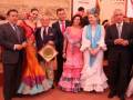 Una familia celebrando un evento tradicional en España, posando con trajes formales y vestidos de flamenca. La imagen muestra un ambiente festivo, con una persona en el centro recibiendo un trofeo.