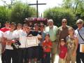 Una imagen de una familia reunida en un cementerio, con un hombre mayor sosteniendo un diploma y otros miembros de la familia posando frente a una cruz.