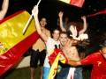 Celebración en un partido de fútbol, con jóvenes vestidos de camisetas rojas y banderas españolas ondeando.