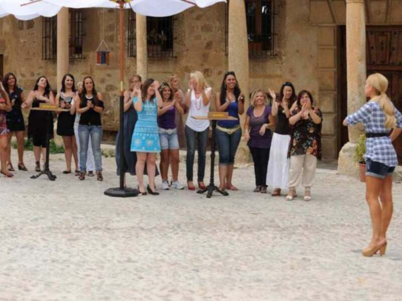 Una escena en un patio con varias personas vestidas de manera casual. Algunas están posando para la foto, mientras que otras observan o esperan su turno. La imagen muestra un ambiente relajado y festivo, con una mezcla de ropa informal.