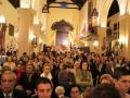 Una multitud de personas en una iglesia, con arcos y vitrales en el fondo.