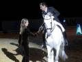 Una niña y un hombre en traje se encuentran con un caballo blanco en una arena de equitación.
