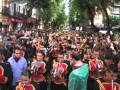 Desfile de músicos en uniforme con instrumentos musicales, entre una multitud en un ambiente festivo.