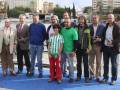 Grupo de personas posando para una foto en una plataforma junto al agua, con edificios y árboles en el fondo.