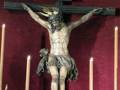 Escultura de Jesús crucificado en una iglesia, rodeado por velas y flores.