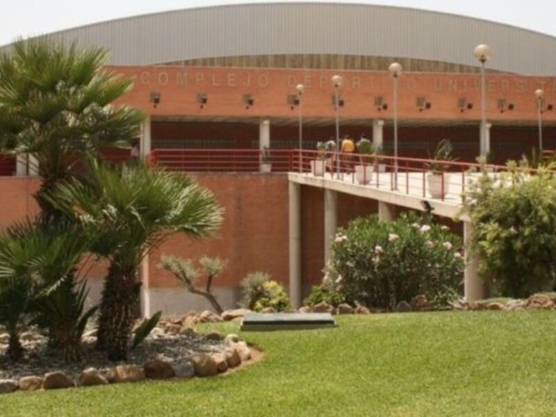 Complejo Deportivo Universitario con arquitectura moderna y jardín con palmeras y flores