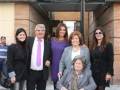 Una familia posa frente a una plaza dedicada a María José Suárez, con un hombre en el centro y cuatro mujeres a su alrededor.
