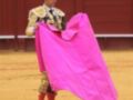 Un torero en traje de luces sostiene un capote rosa en el ruedo de una corrida de toros.