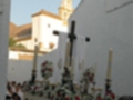 Procesión religiosa con estandartes y cruces en una calle de pueblo blanco.