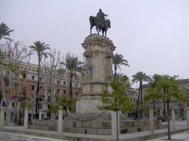Estatua ecuestre de un hombre en una plaza con palmeras y edificios en el fondo.