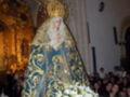 Imagen de una Virgen María en un altar dorado, rodeada por fieles y flores blancas.