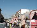 Desfile de carrozas tradicionales en una calle de ciudad, adornadas con flores y mantas coloridas.