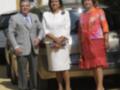Tres personas posan frente a un vehículo, dos mujeres y uno hombre. Una de las mujeres sostiene una bolsa con un sobre. La escena parece ser formal o ceremonial, posiblemente en una ceremonia de premiación.