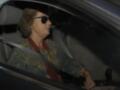 Una mujer con gafas de sol y chaqueta estampada sentada en el asiento del conductor de un coche.