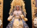 Imagen de una estatua de la Virgen María con vestimentas azules y doradas, coronada y rodeada de flores blancas.