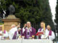 Celebración religiosa en un entorno verde con una estatua en el fondo.