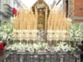 Procesión de Semana Santa con imagen de la Virgen María en un paso ornado con candelabros y flores blancas.