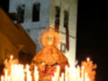 Procesión nocturna con velas y imagen religiosa en un entorno histórico.