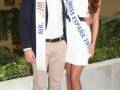 Miss España 2017 y su acompañante en un evento formal. La mujer lleva un vestido blanco con un gran corbatín de sash y el hombre está con un traje formal y corbata. Ambos sonríen para la foto.