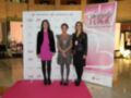 Tres mujeres posan frente a un póster de "Beauty Fever" en un evento de belleza. La imagen muestra una alfombra roja con logotipos de marcas y un fondo blanco con letras en verde. La escena se desarrolla en un entorno interior, posiblemente dentro de un hotel o centro comercial.