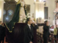 Una procesión religiosa con una imagen venerada en un altar, rodeada de flores y acompañada por dos hombres vestidos formalmente.