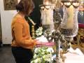 Una mujer vestida con un vestido amarillo y negro, posa junto a un altar adornado con velas y flores blancas. El ambiente es festivo y el altar destaca por su elaboración y lujo.