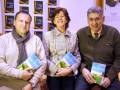 Tres personas sonrientes sostienen libros titulados "El Almazar". La imagen está firmada por Casa del Libro.