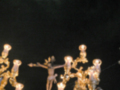 Imagen nocturna de una procesión religiosa con un crucificado y candelabros dorados. El cielo está cubierto por una nube de luz brillante, posiblemente un meteorito o estrella fugaz.