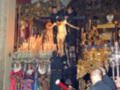 Una imagen de una iglesia con un altar dorado y velas encendidas. En el centro, hay personas vestidas con trajes tradicionales celebrando una ceremonia religiosa. En la parte inferior, un hombre toca el violín mientras otros asisten a la celebración. La atmósfera es festiva y reverente, reflejando el significado cultural de la ceremonia.
