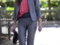 Una mujer con un look elegante y profesional, vestida con una blazer gris, una camiseta rosa y pantalones grises.