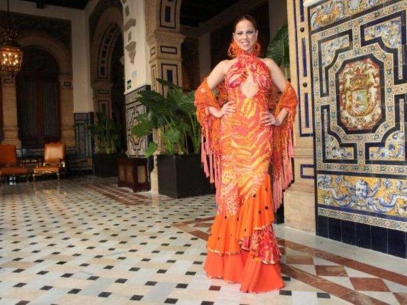 Elegante mujer en traje de flamenca, posando en un vestíbulo con azulejos de cerámica tradicional.