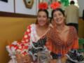 Dos mujeres vestidas con trajes de flamenca sonríen en un ambiente festivo.