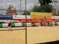 Un hombre con una gorra roja y un chaleco negro juega tenis en una cancha de arena, con un muro de anuncios de Coca-Cola y Club Náutico Sevilla al fondo.