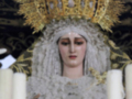Representación religiosa con vestimenta blanca y corona dorada, rodeada de velas blancas.