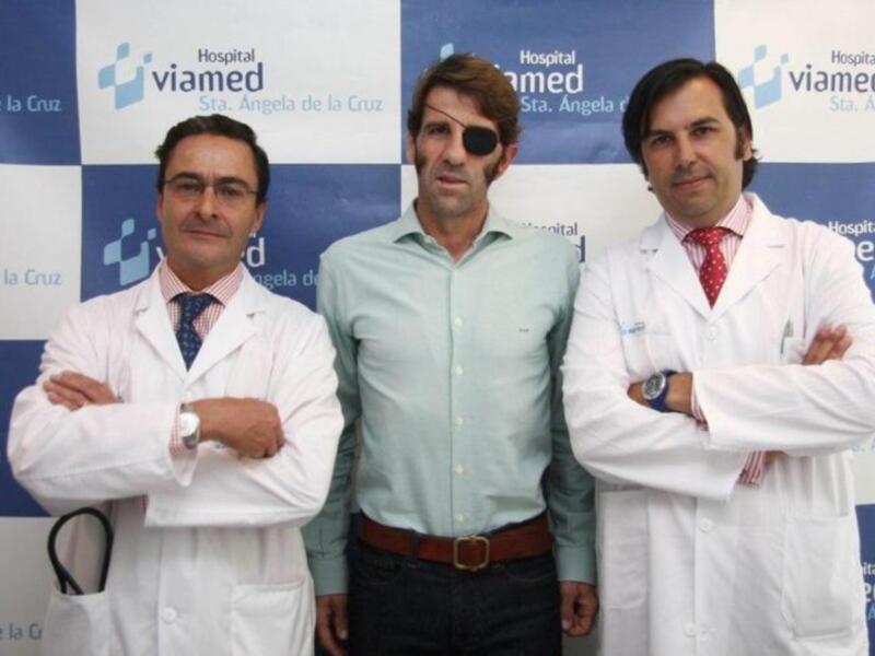 Tres médicos posan frente a un fondo azul con logos de viamed. El médico en medio lleva una camisa verde y un cinturón marrón, mientras que los otros dos están en ropa blanca.
