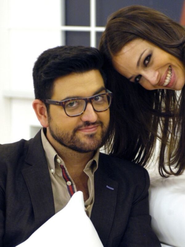 Un hombre con una camisa blanca y un chaleco negro, junto a una mujer con el cabello largo y una sonrisa. Ambos están en un entorno interior, posiblemente una oficina o estudio.