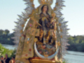 Imagen de una Virgen María con un halo de cristales, vestida en negro y dorado, rodeada por fieles.