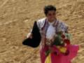 Matador celebrando en la plaza de toros, sosteniendo flores y un sombrero negro.