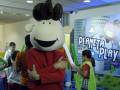 Un personaje con orejas y cuernos, vestido de rojo, se encuentra entre niños en un entorno infantil con una pantalla de "Planeta Play".