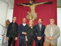 En un ambiente religioso, cuatro personas posan frente a una estatua de Jesús crucificado en el centro. La imagen es parte del contexto de un evento o celebración religiosa.